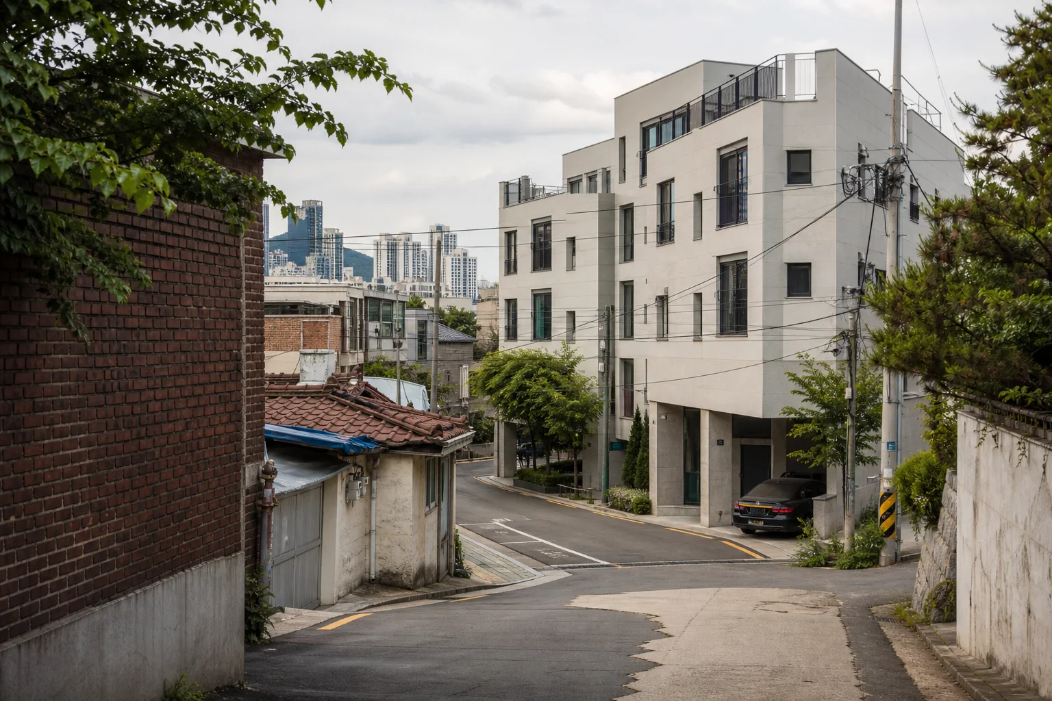 오래된 벽돌 담장과 저층 주택 골목 건너편에 새로 지은 흰색 공동주택이 마주한 서울 주거지 경계