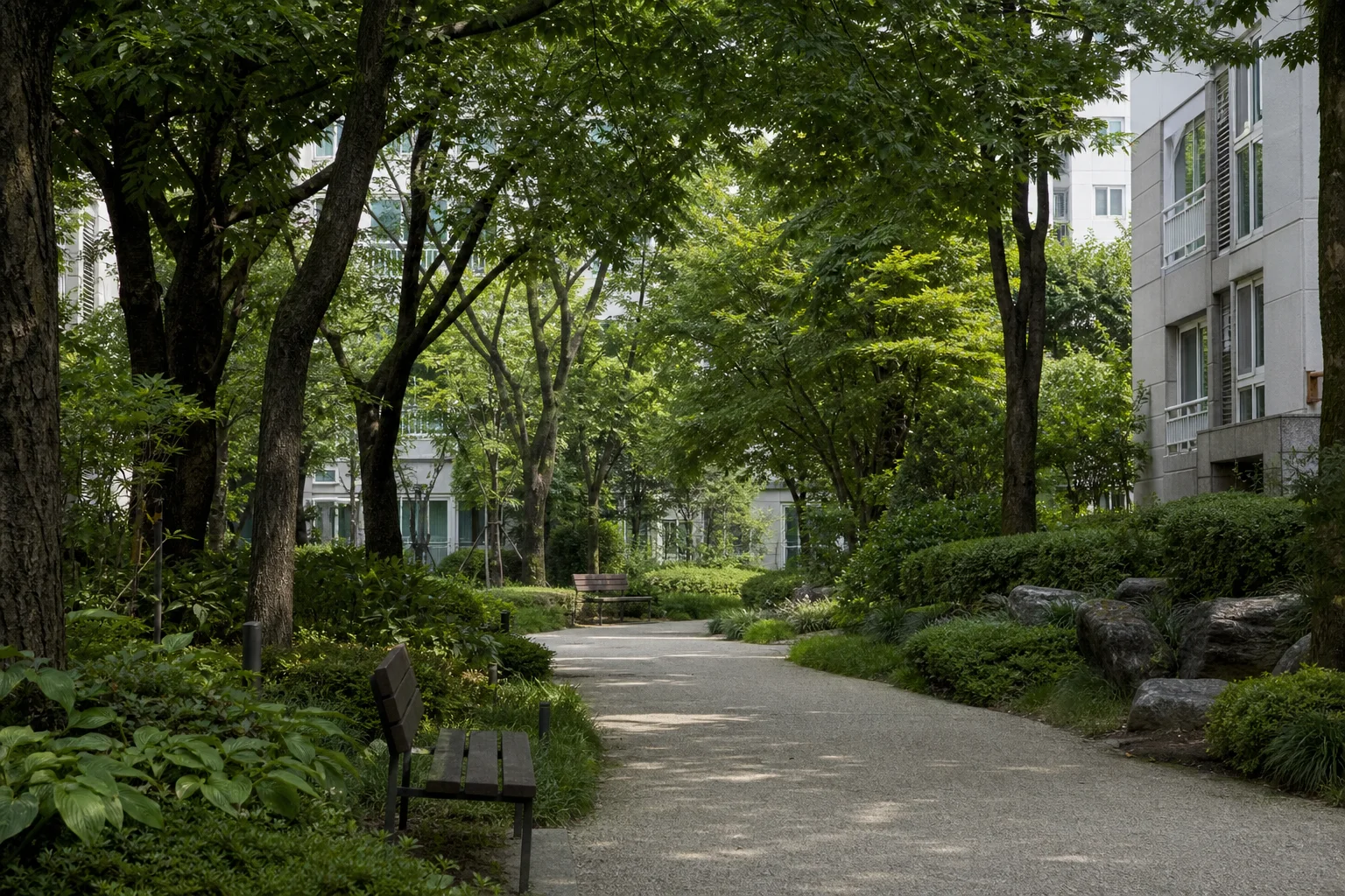 성숙한 나무와 관목, 완만하게 굽은 산책로와 벤치가 아파트 건물 사이를 연결하는 녹지 통로