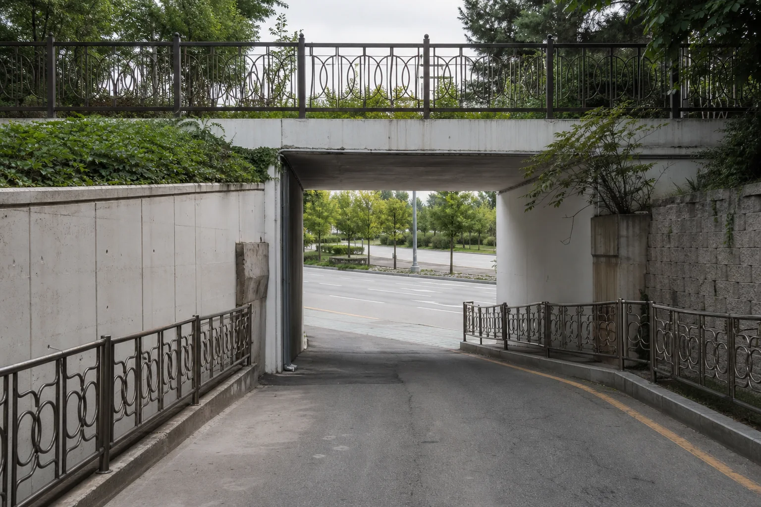 좁은 주택가 길이 낮은 보행 통로 아래를 지나 넓고 나무가 심어진 도로로 연결되는 모습